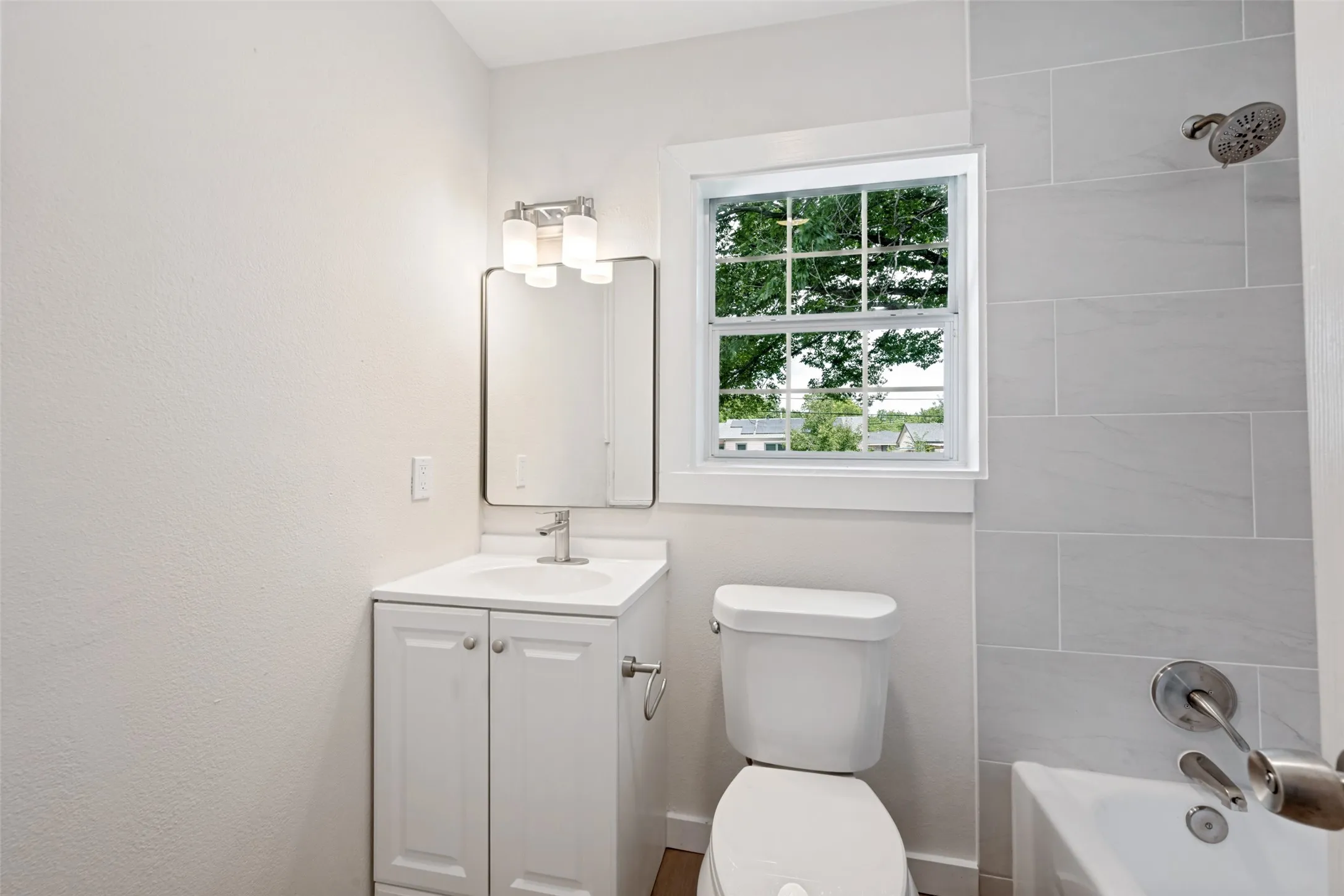 Bright, updated bathroom featuring a white vanity with dual-door cabinetry, ceramic sink, chrome fixtures, and ample counter space