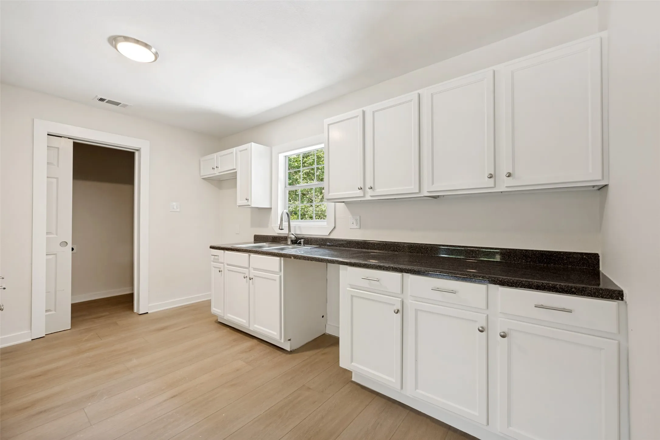 Kitchen area featuring white cabinetry, dark countertops, a double basin sink with a high-arc faucet, and wood-finish flooring