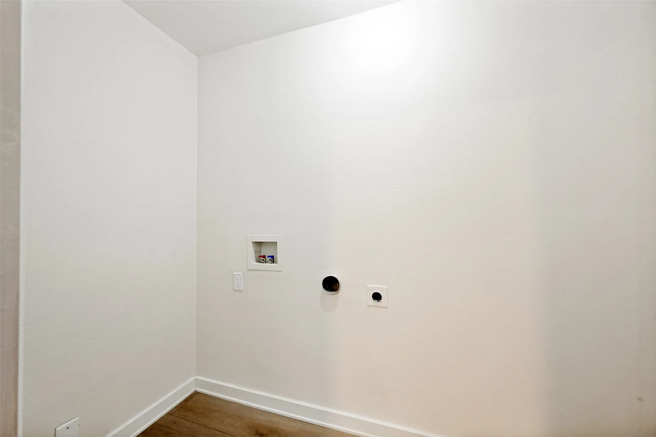 Utility area with wood-finish flooring, white baseboards, and a dedicated laundry hookup