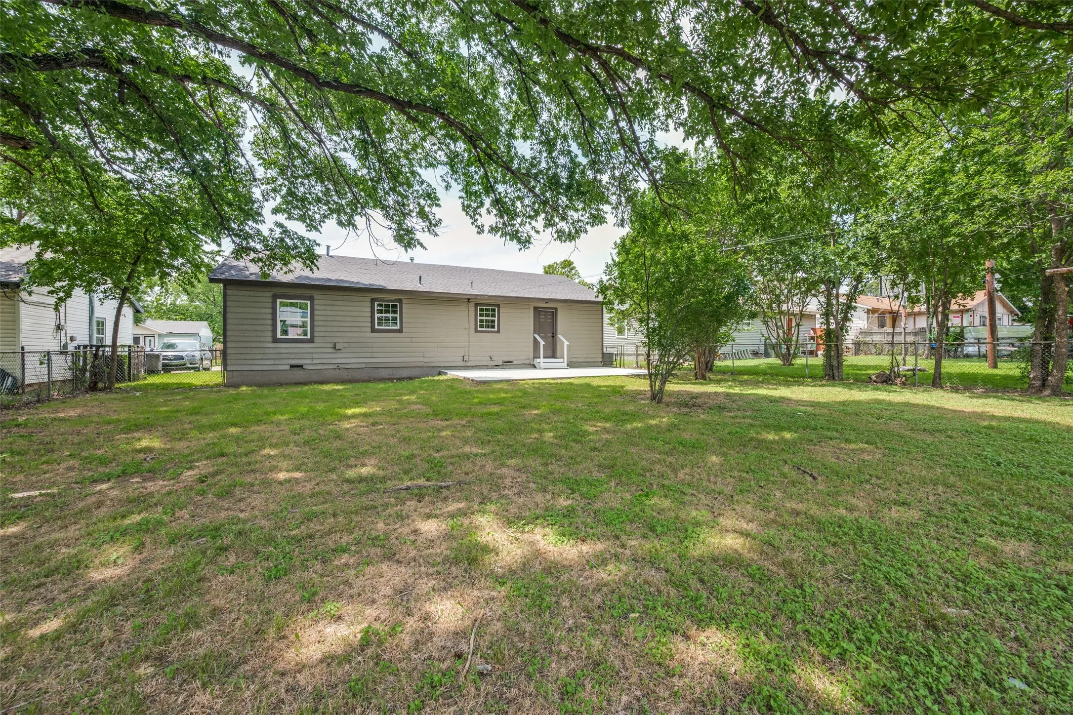 Expansive rear yard featuring a concrete patio, mature trees, and a chain-link fence
