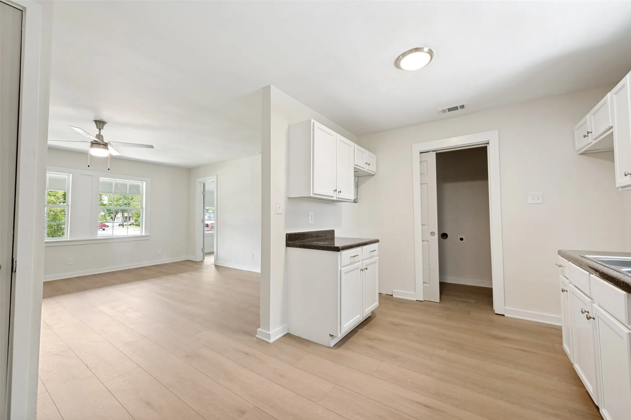 Kitchen and living area featuring light wood-finish flooring, white cabinetry, dark countertops, and a ceiling fan