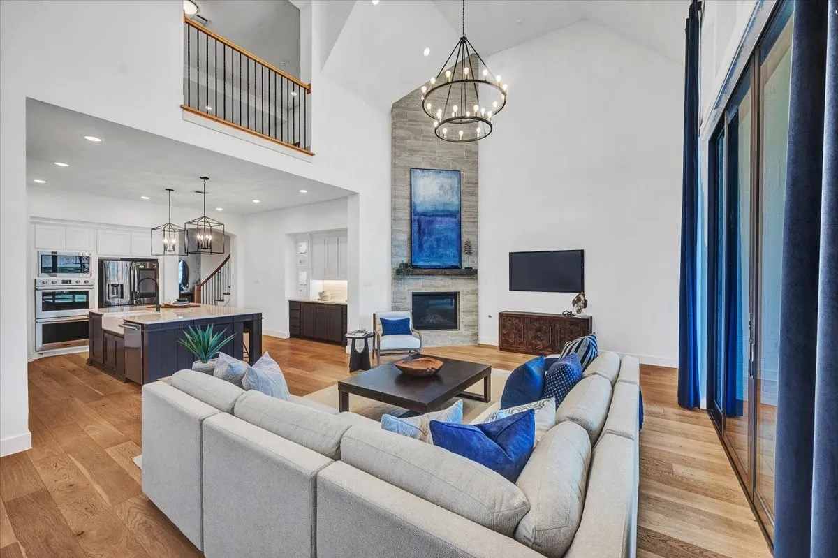 Vaulted living area featuring a stone fireplace, wood-finish flooring, and a large multi-pane glass door