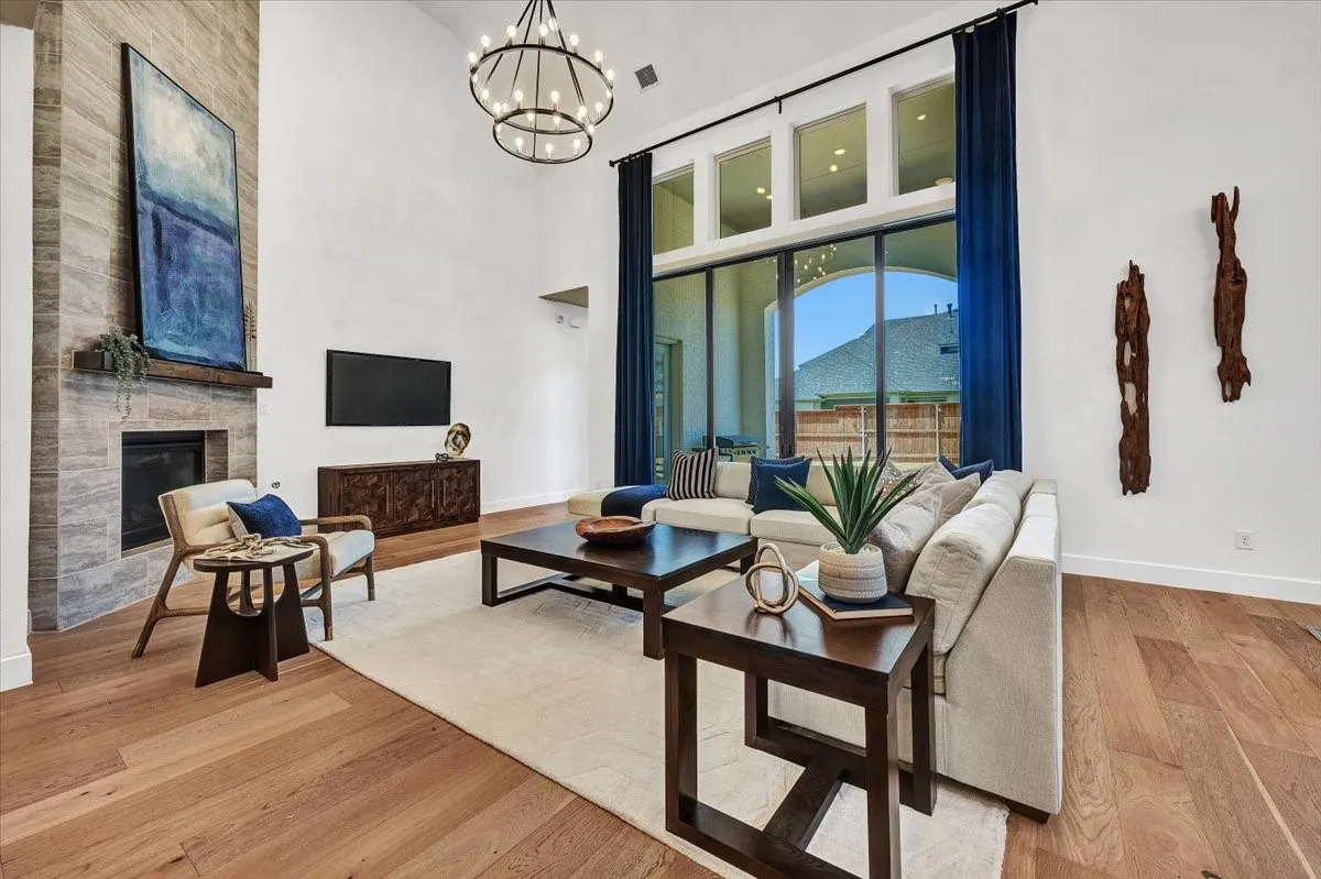 Spacious living area featuring double-height ceilings, a stone-clad fireplace with a wood mantel, and expansive windows