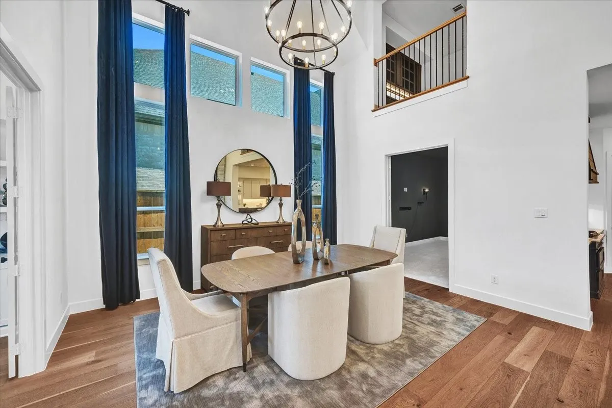 Double-height ceiling dining area featuring wood-finish flooring, a contemporary chandelier, tall windows, and a second-story interior balcony with dark metal railings