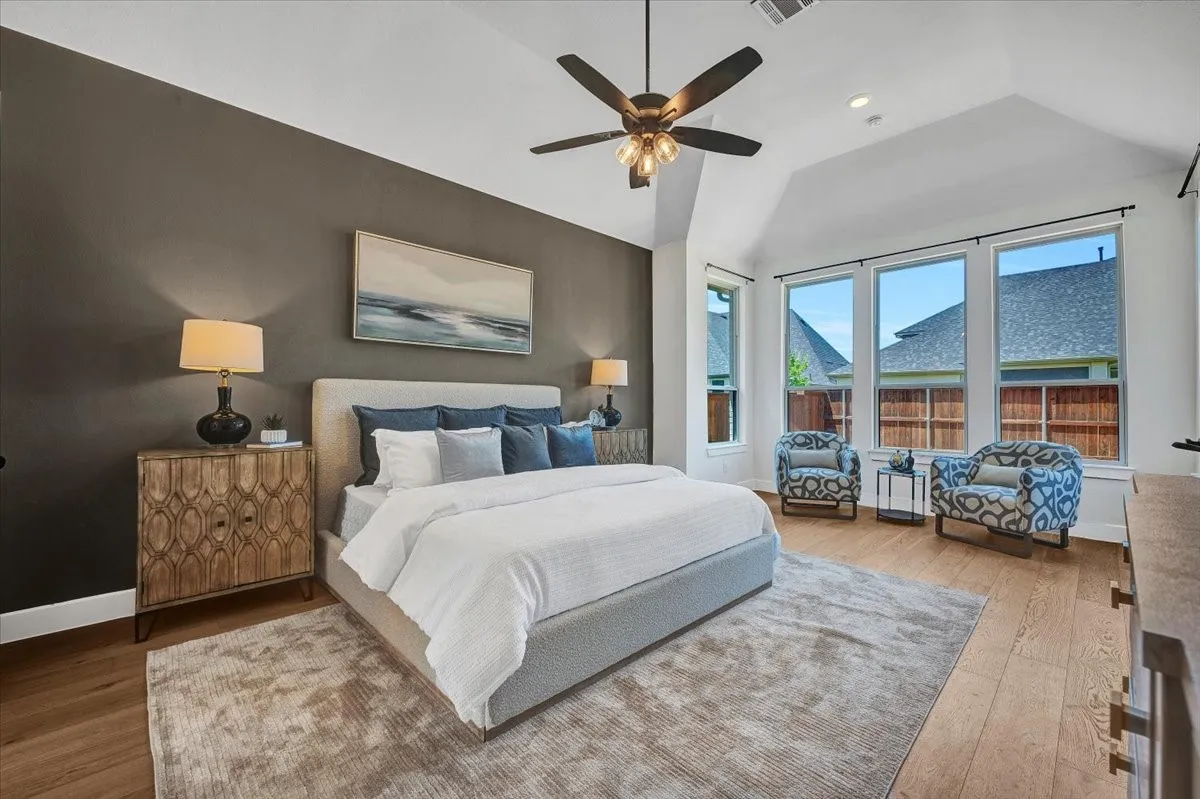 Vaulted ceiling bedroom featuring wood-finish flooring, large picture windows, and a ceiling fan with integrated lighting