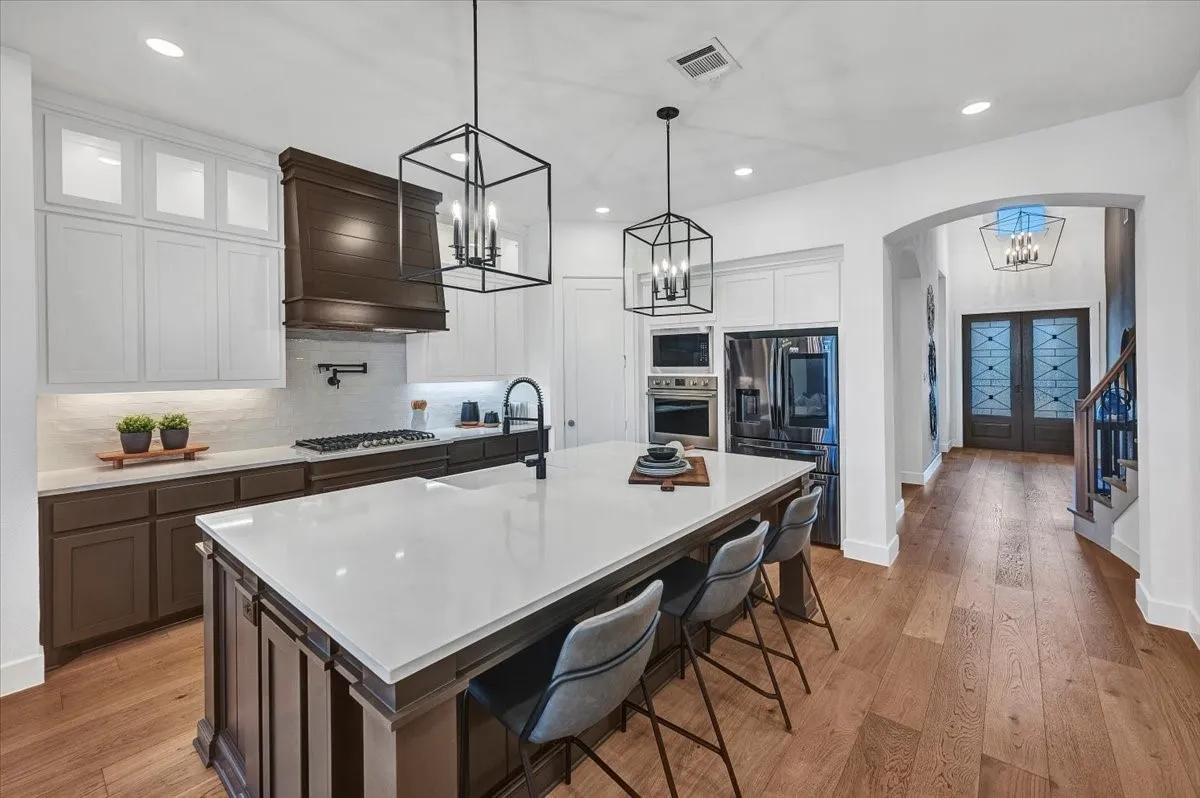 Kitchen featuring a large island with a light-toned countertop, dark wood-finish cabinetry, stainless steel appliances, and wood-finish flooring