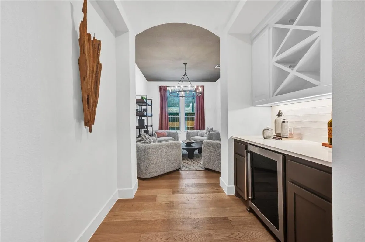 Dedicated wet bar featuring dark wood-finish cabinetry, a beverage refrigerator, and a white countertop with a tiled backsplash. Leads into flex space that can be used as a formal dining, library, sitting room, secondary office, or even a dedicated mahjong room.