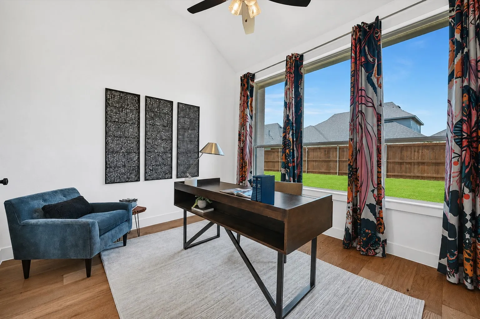 digitally enhanced -Bright room featuring a vaulted ceiling with a ceiling fan, large windows, wood-finish flooring, and a fenced backyard