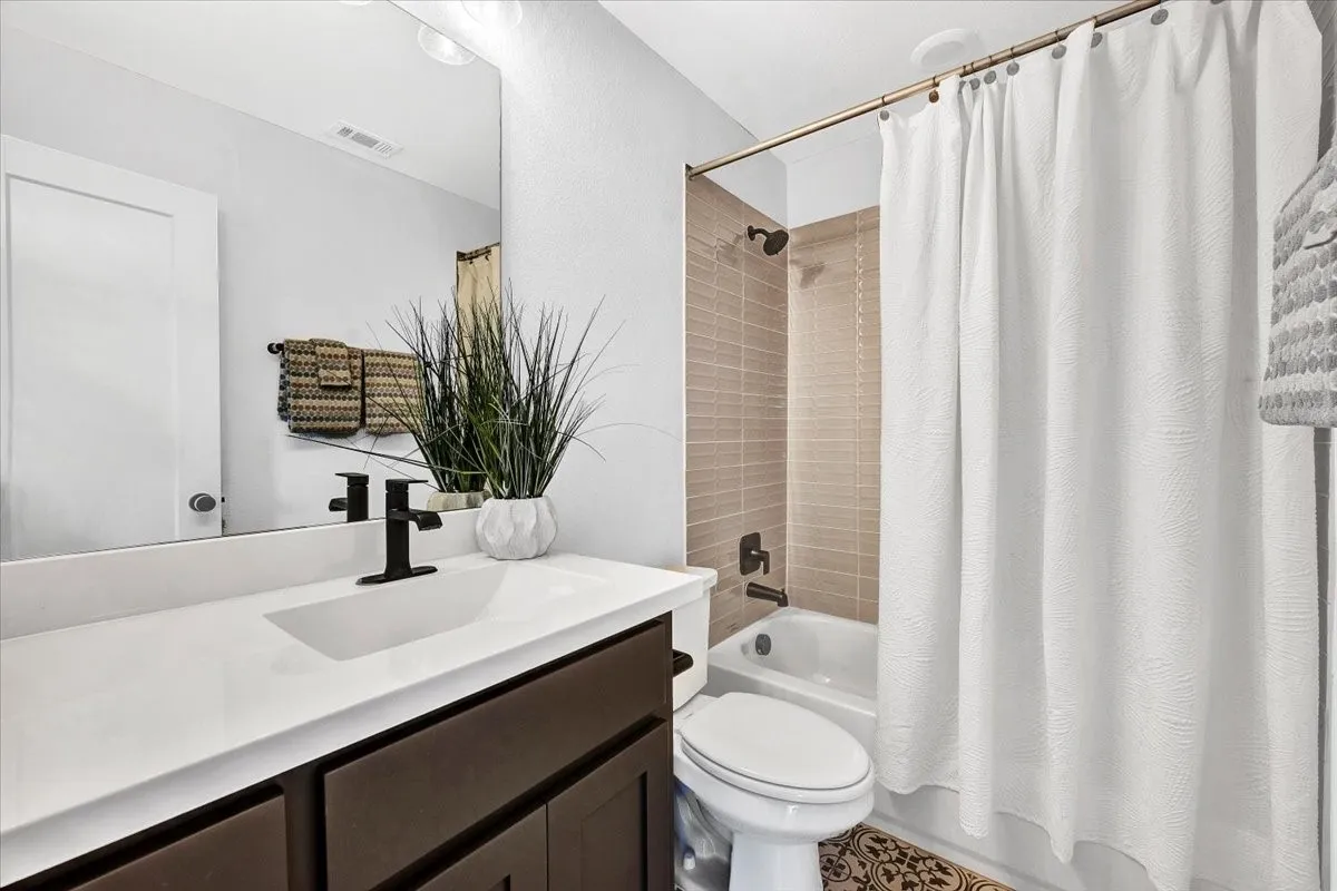 Contemporary bathroom featuring a dark wood-finish vanity with a white countertop and integrated sink, matte black faucet, and a large wall mirror