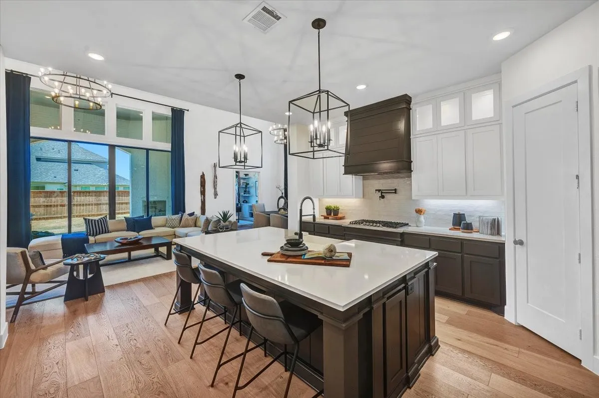 Open-concept kitchen and living area featuring wood-finish flooring, a kitchen island with seating, pendant lighting, white upper cabinetry, and dark lower cabinetry with a matching range hood