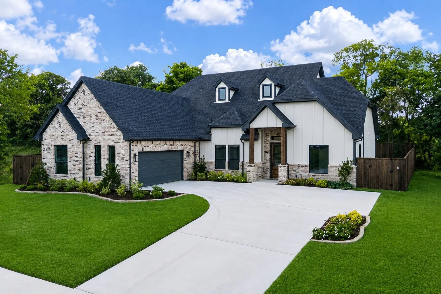 Modern farmhouse exterior featuring a stone and vertical siding facade, a dark shingle roof, a two-car garage, and a concrete driveway