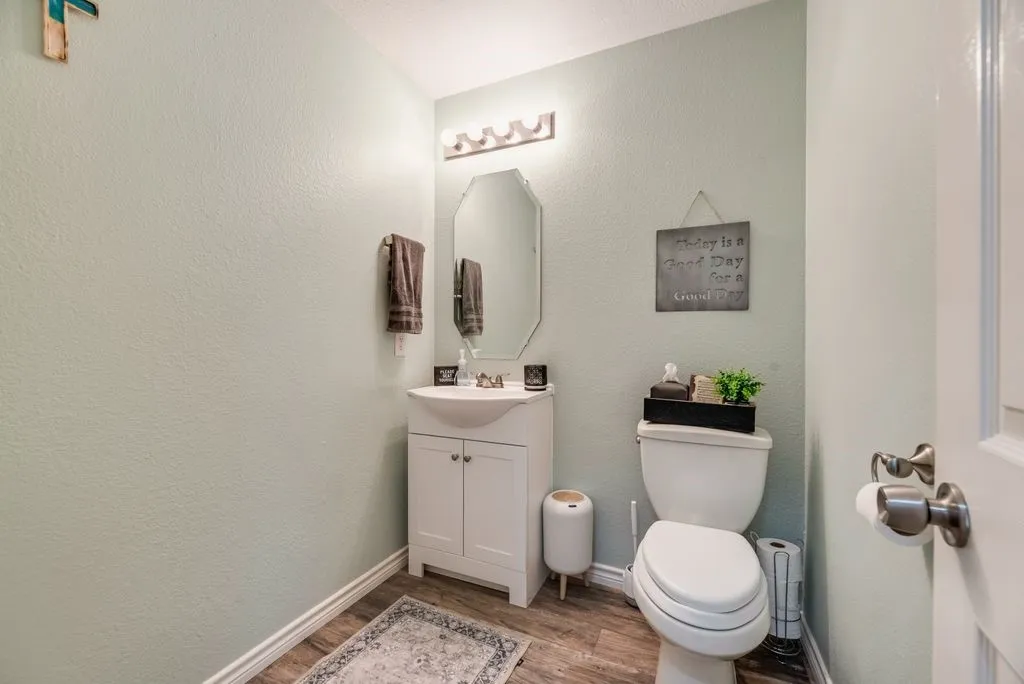 Powder room featuring a white vanity with integrated sink, wood-finish flooring, and a wall-mounted mirror