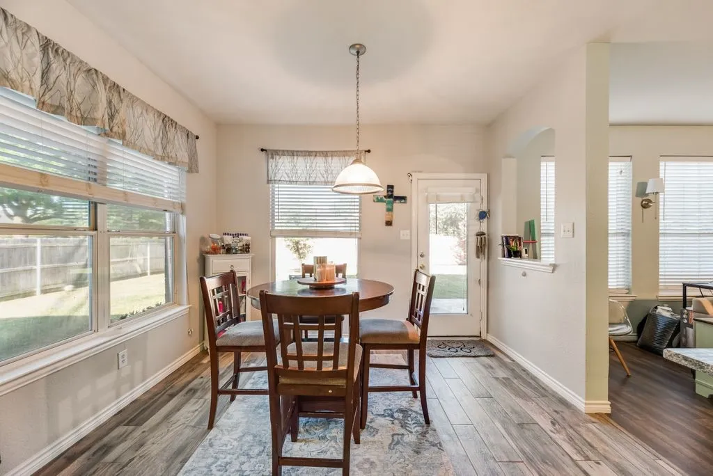 Dining area featuring wood-finish flooring, a contemporary pendant light fixture, and multiple windows with blinds