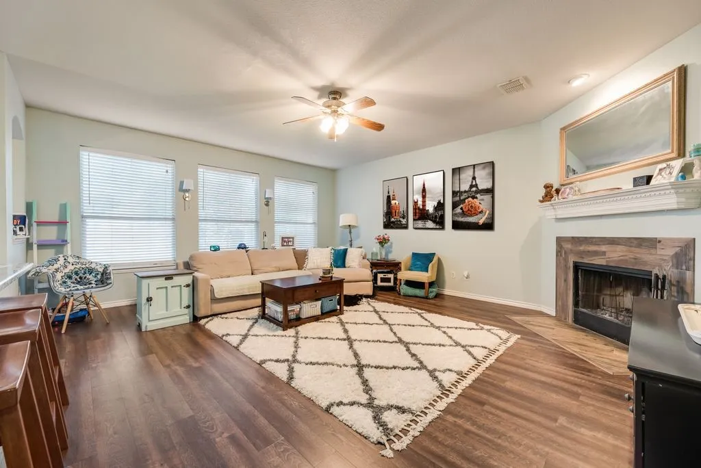 Spacious living area featuring wood-finish flooring, a ceiling fan, and multiple windows with blinds