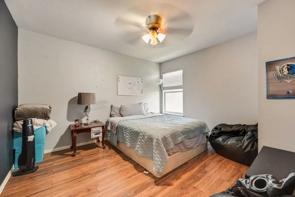 Room featuring wood-finish flooring, a ceiling fan with integrated lighting, and a window with blinds