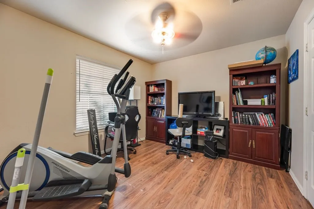 Room featuring wood-finish flooring, a ceiling fan with integrated lighting, and a window with blinds