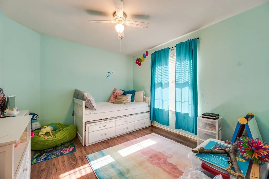 Bright interior room featuring wood-finish flooring, a ceiling fan with integrated lighting, and a window with blinds