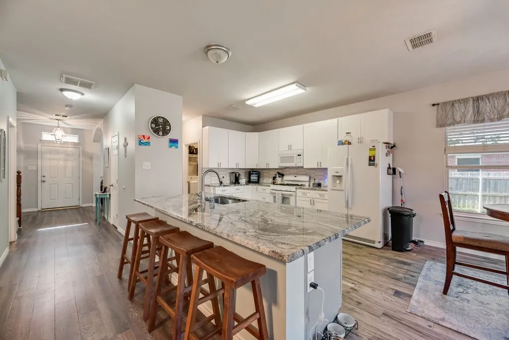 Open-concept kitchen featuring a large island with seating, granite countertops, white cabinetry, integrated stainless steel appliances, and wood-finish flooring
