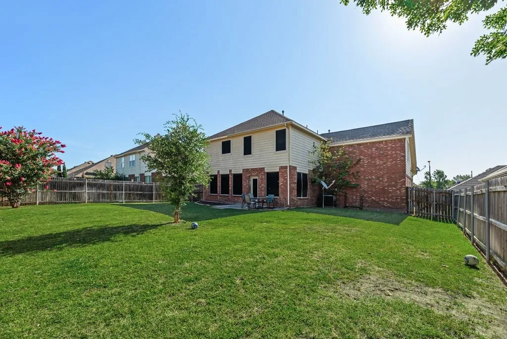 Expansive backyard featuring a manicured lawn, full privacy fencing, and mature trees