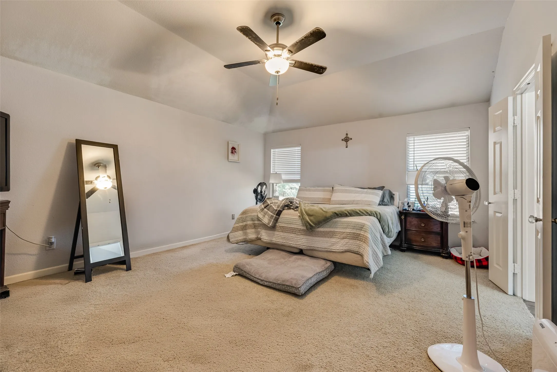 Carpeted bedroom featuring a vaulted ceiling with a ceiling fan, two windows with blinds, and white paneled doors
