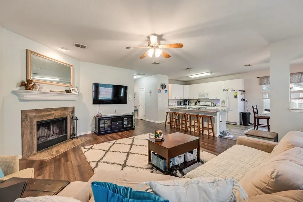 Open-concept living area featuring wood-finish flooring, a fireplace with a stone-look surround and white mantel, and a ceiling fan