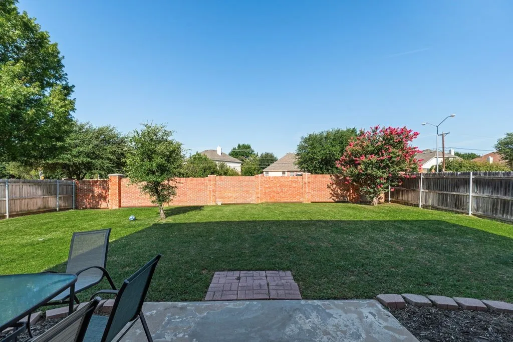 Spacious backyard featuring a concrete patio, brick paver accents, and a large grassy area