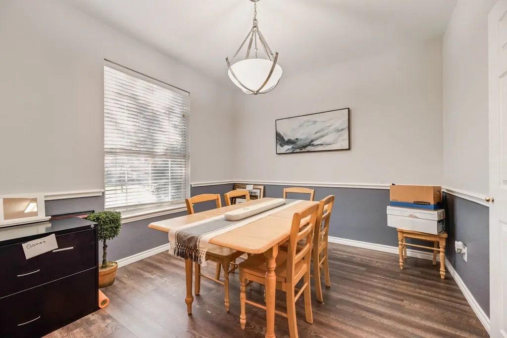 Dining area featuring wood-finish flooring, a contemporary chandelier, two-tone wall treatment with chair rail molding, and a large window with horizontal blinds