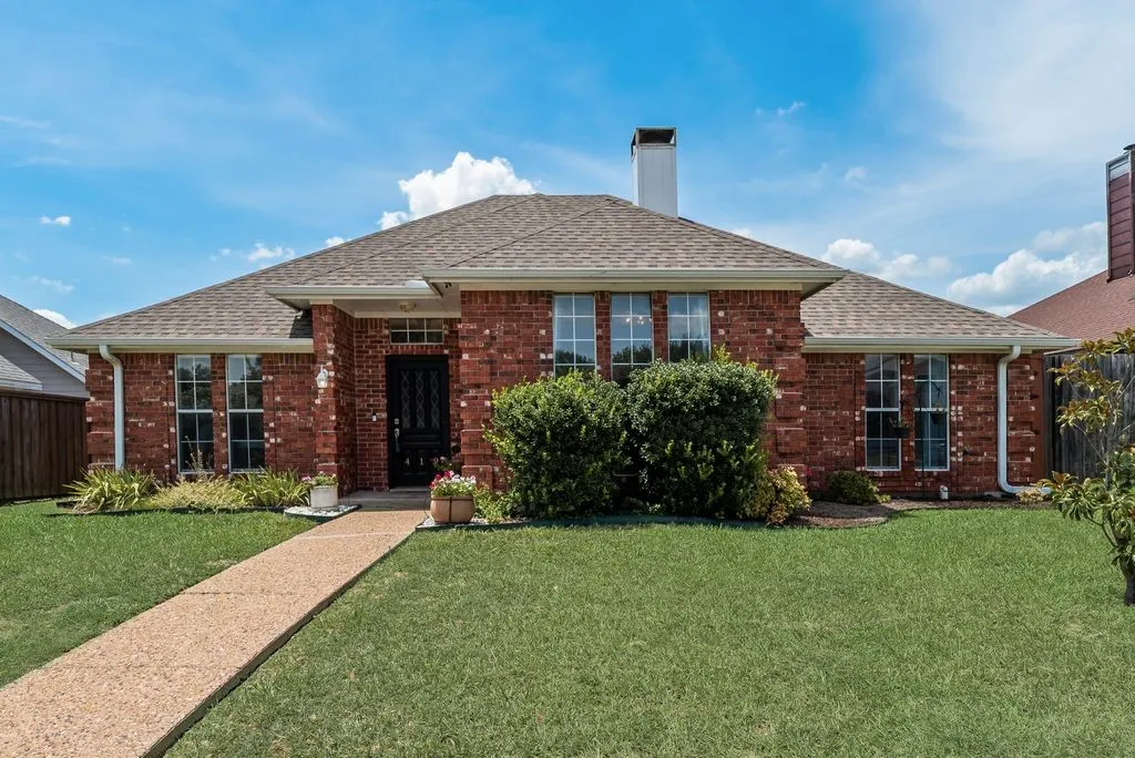 Brick exterior featuring a gabled roofline, a front lawn, a paved walkway, and mature landscaping