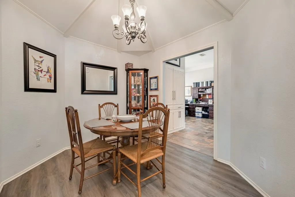 Vaulted ceiling with an ornamental chandelier, wood-finish flooring, and white baseboards