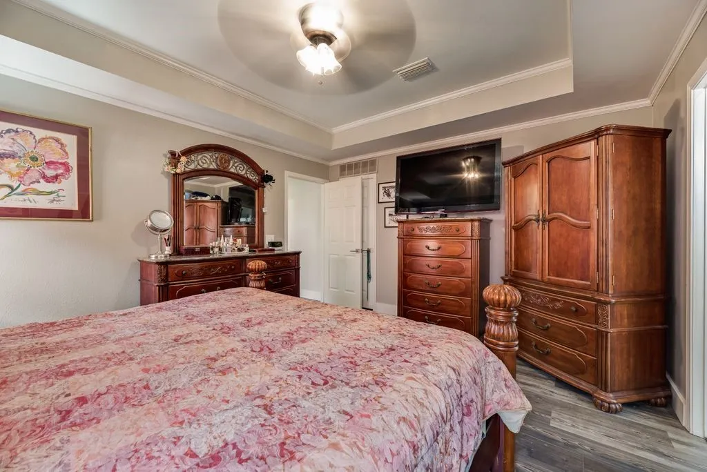 Tray ceiling with crown molding, wood-finish flooring, and a ceiling fan with light fixture