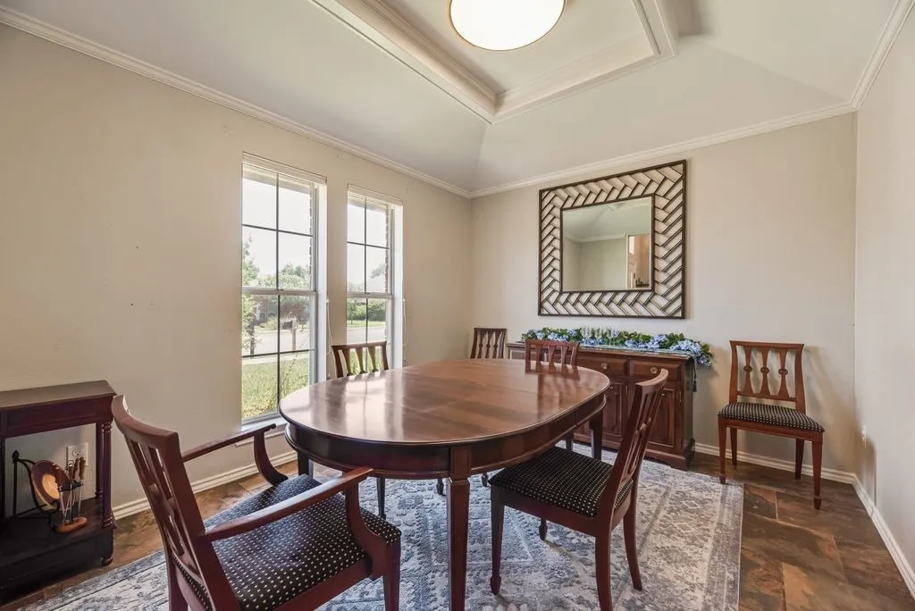 Dining area featuring wood-finish flooring, two large windows, a tray ceiling with crown molding, and a built-in buffet with a stone top