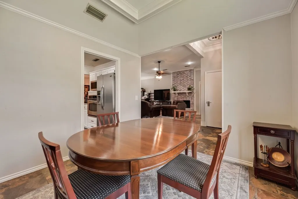 Dining area featuring crown molding and an open pass-through to a living space with a brick-surround fireplace