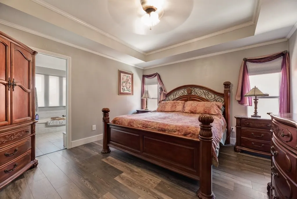 Bedroom featuring wood-finish flooring, tray ceiling with fan, and crown molding