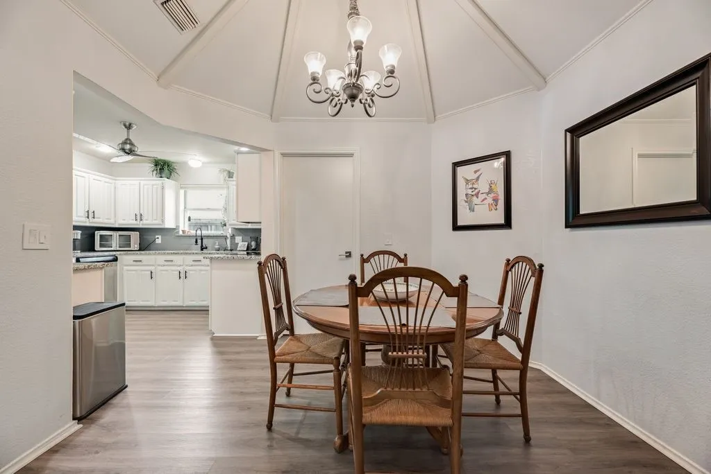 Open-concept dining area featuring a vaulted ceiling with exposed beams, central chandelier, and wood-finish flooring