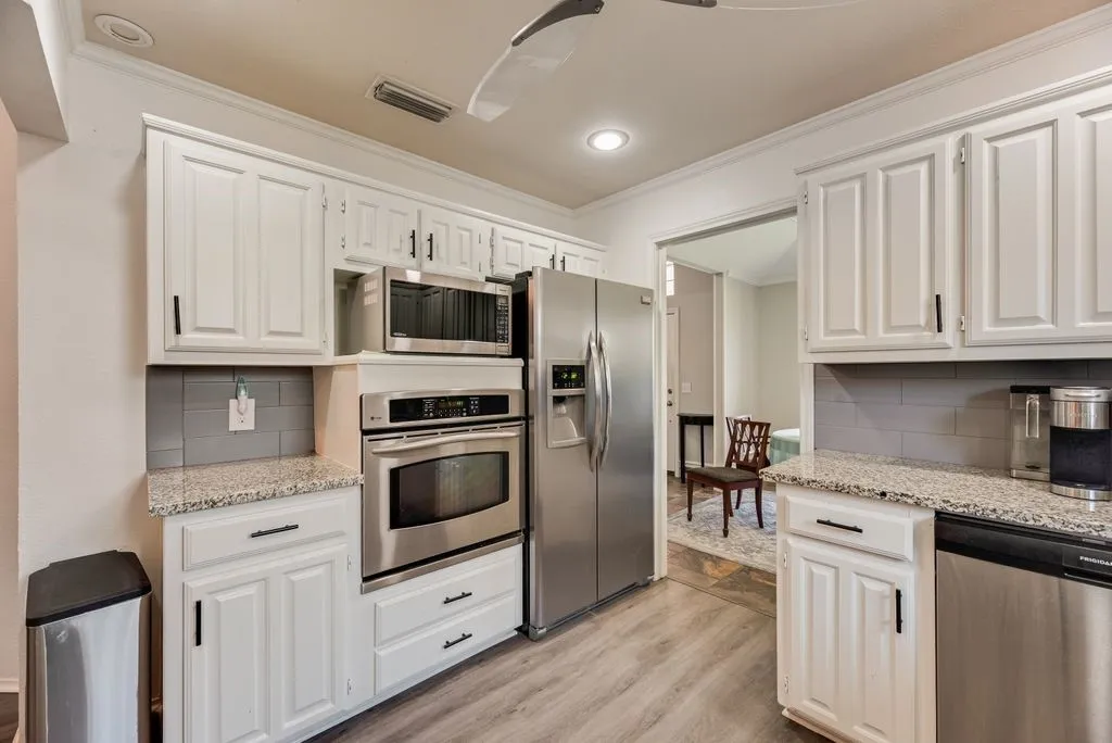 Contemporary kitchen featuring white cabinetry, stainless steel appliances, granite countertops, a gray subway tile backsplash, and wood-finish flooring