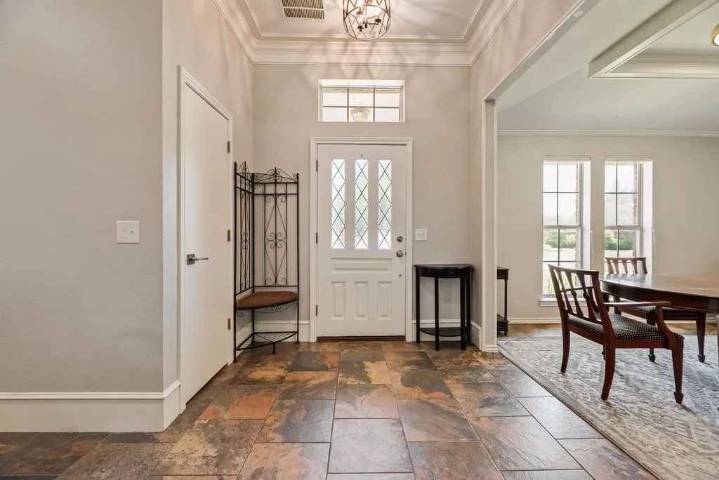 Foyer featuring natural stone tile flooring, a white paneled entry door with decorative glass inserts, and a transom window
