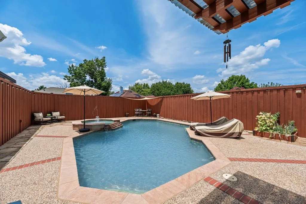 Private backyard featuring an in-ground swimming pool with an integrated spa, exposed aggregate concrete decking with brick accents, and a perimeter privacy fence