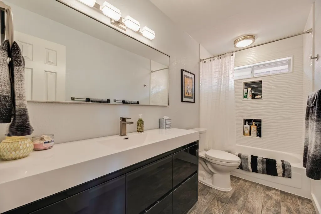Bathroom featuring a wide vanity with dark cabinetry, an integrated sink, and wood-finish flooring
