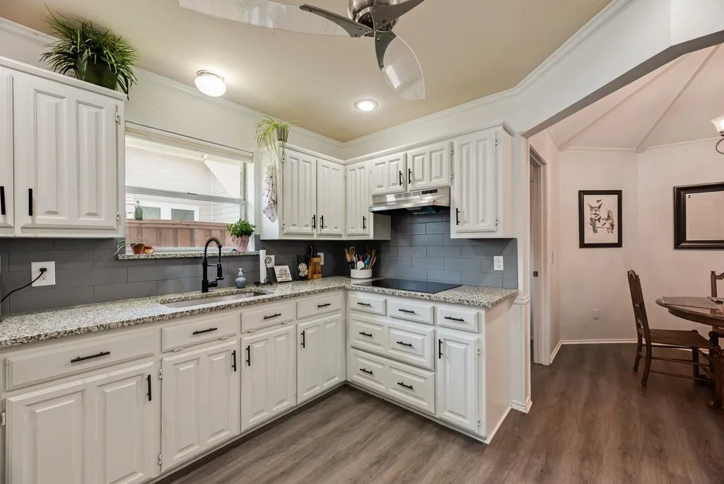 Kitchen featuring white cabinetry, speckled countertops, gray subway tile backsplash, and wood-finish flooring
