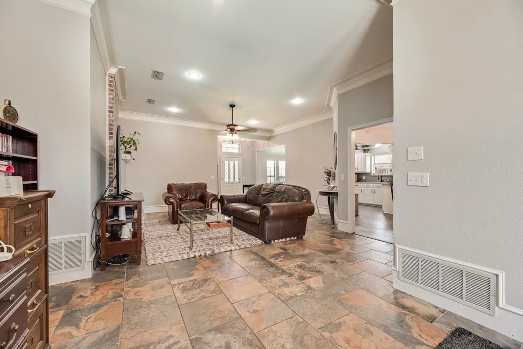 Living area featuring large format stone tile flooring, crown molding, recessed lighting, and a ceiling fan