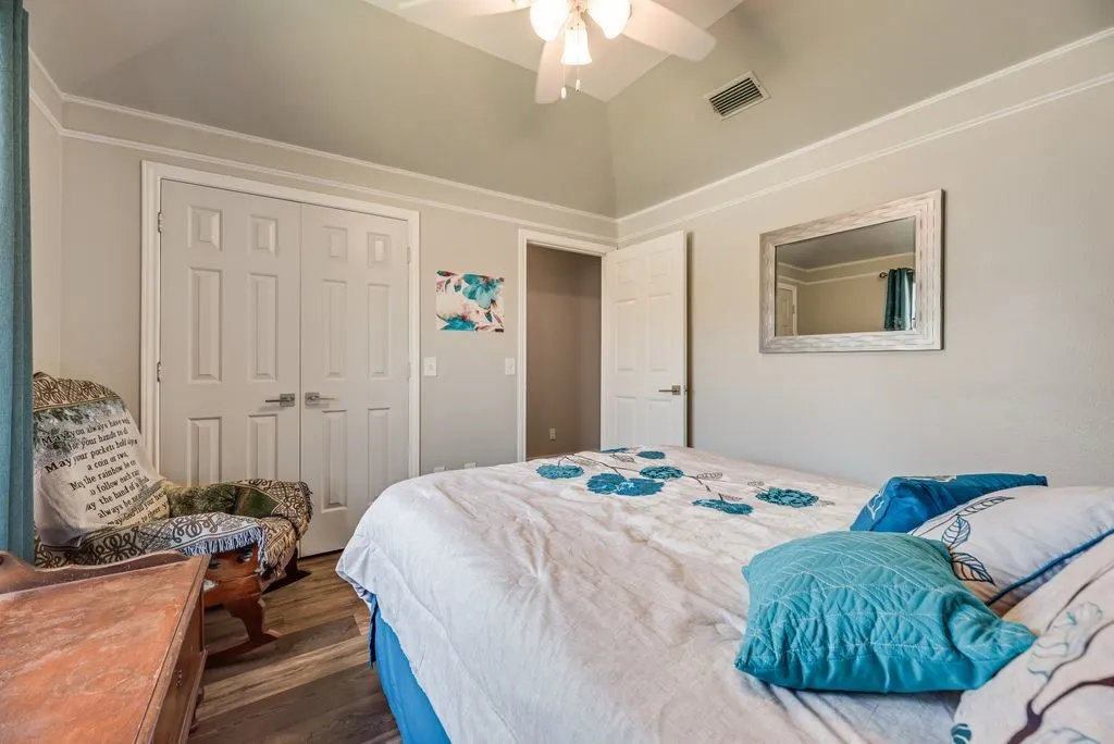 Vaulted ceiling with crown molding, ceiling fan, wood-finish flooring, paneled doors, and light neutral wall paint