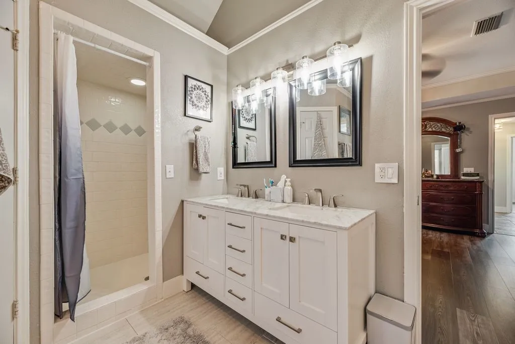 Bathroom featuring a double vanity with white cabinetry and a light-toned countertop, dual rectangular mirrors, and a shower with subway tile surround and decorative accents