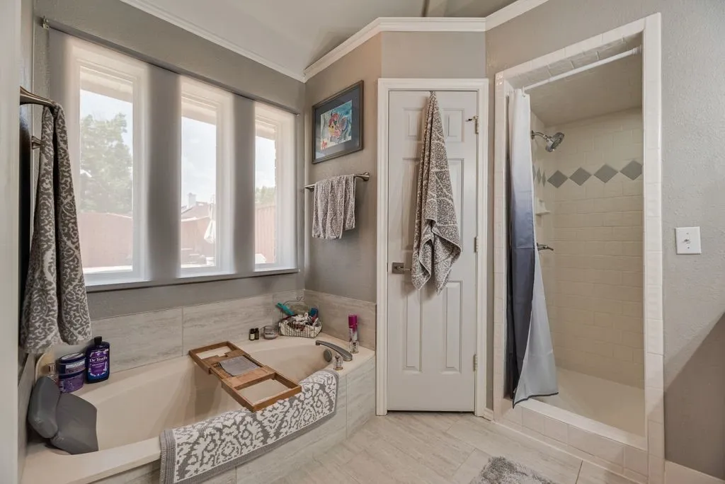 Soaking tub with a tiled surround, three large windows, and a separate shower with a decorative tile band