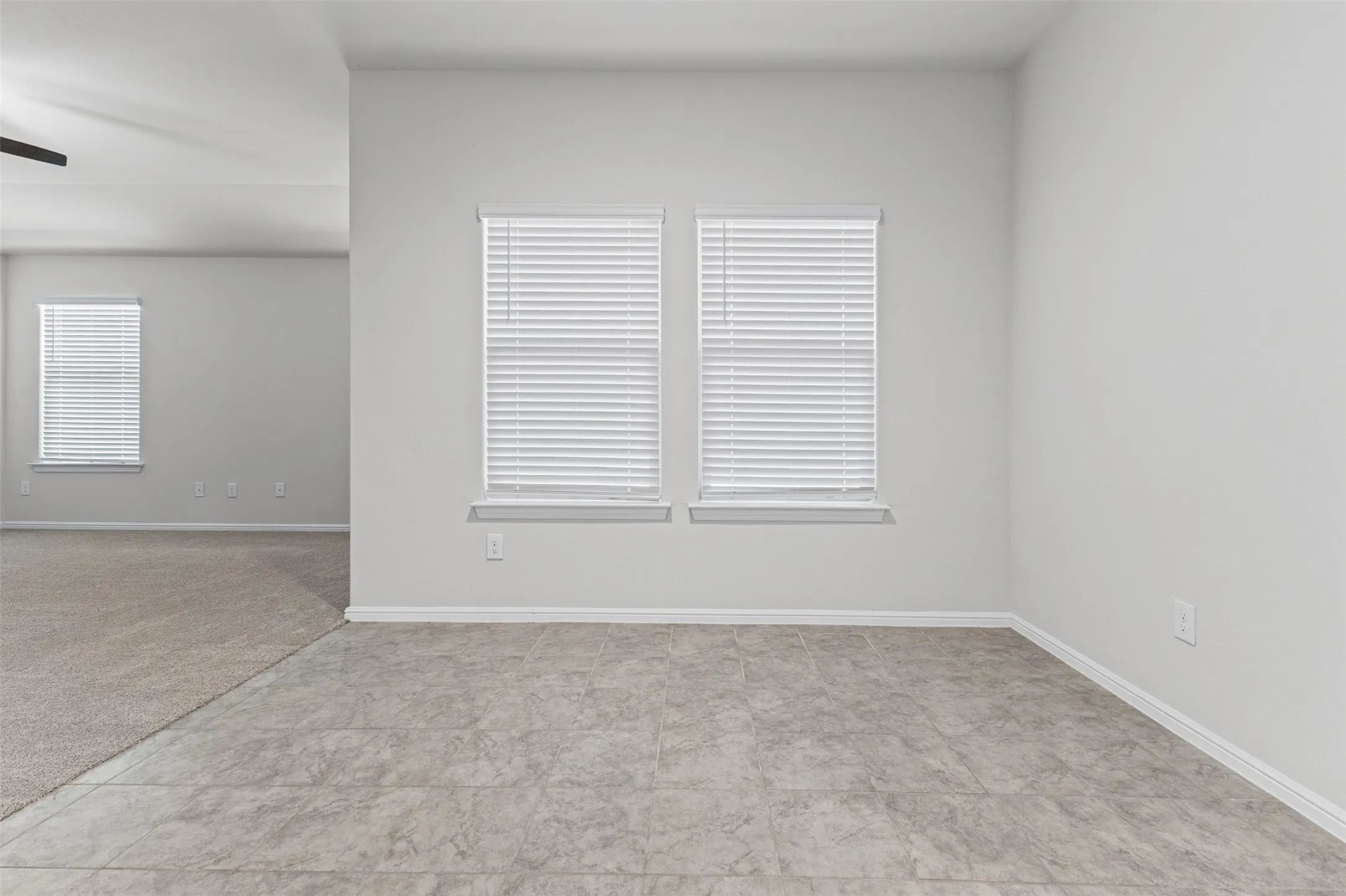 Neutral-toned interior with patterned tile flooring and two windows featuring horizontal blinds