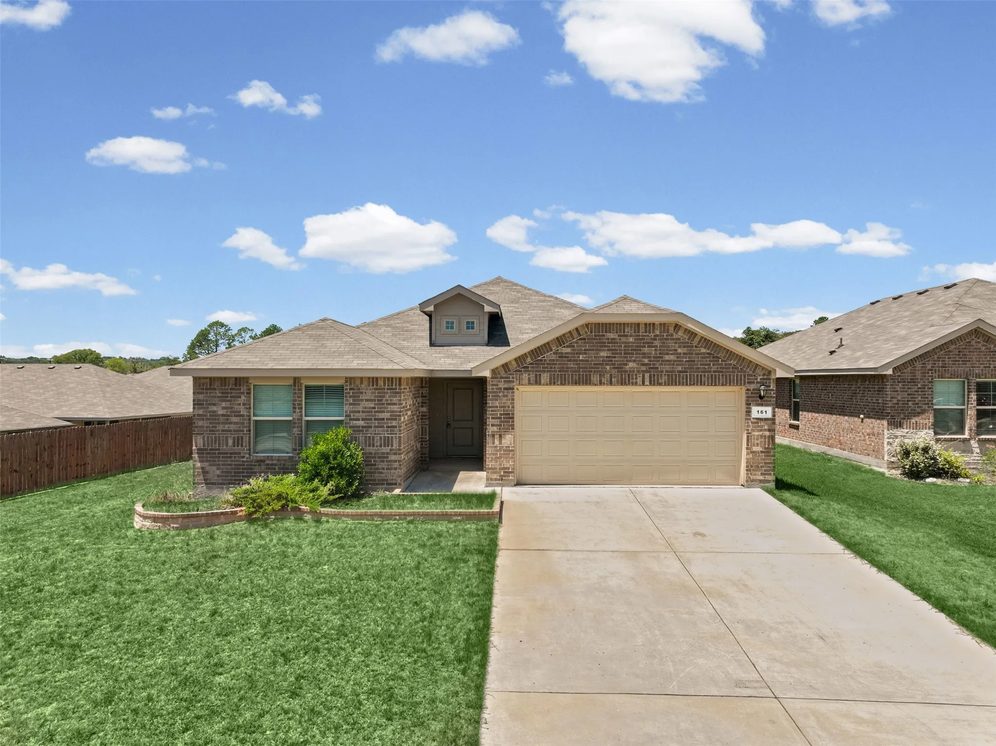 Brick facade home featuring a two-car garage, front yard landscaping, and a pitched roof
