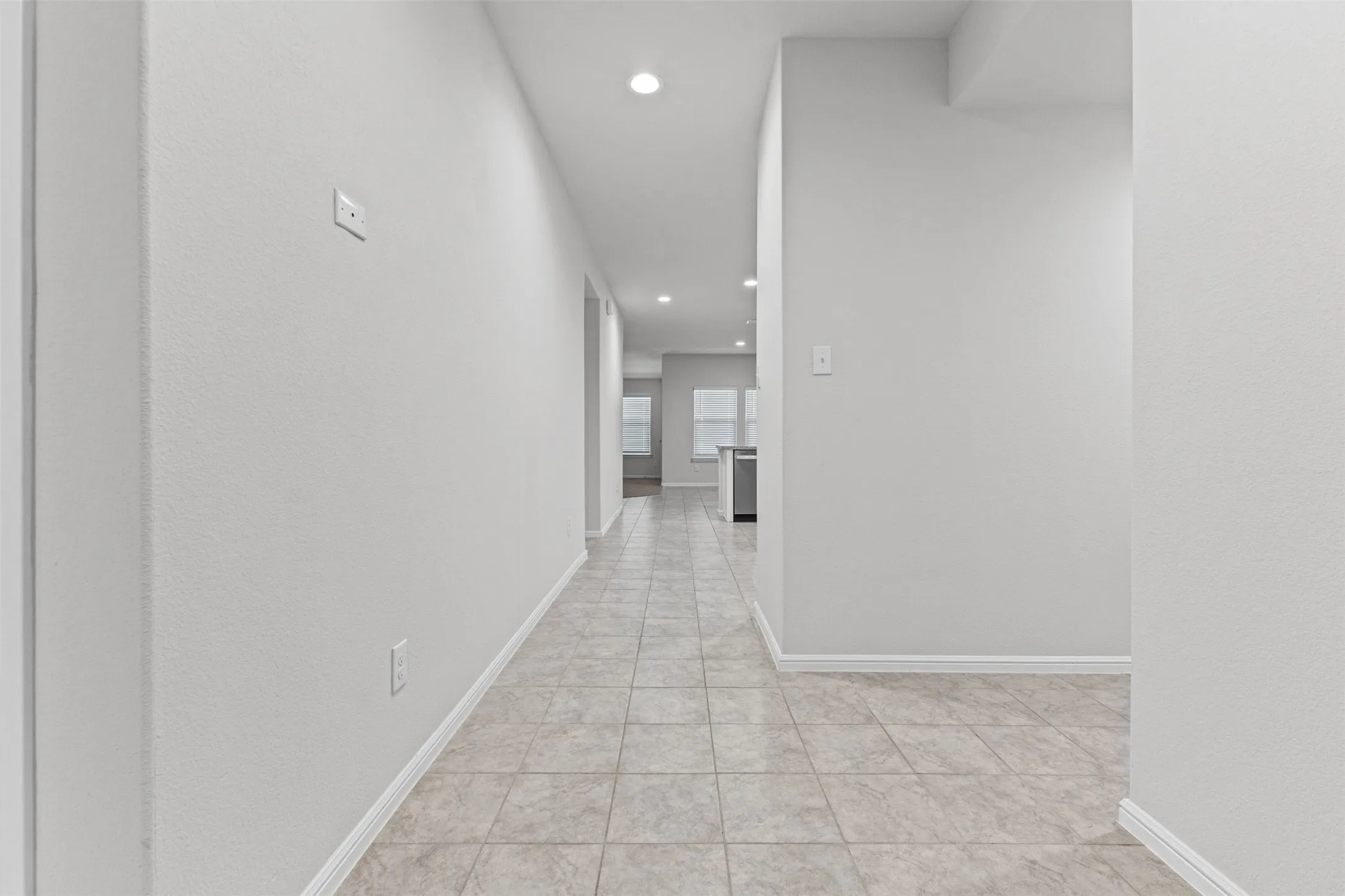 Long hallway featuring light-toned square tile flooring, recessed lighting, and white baseboards