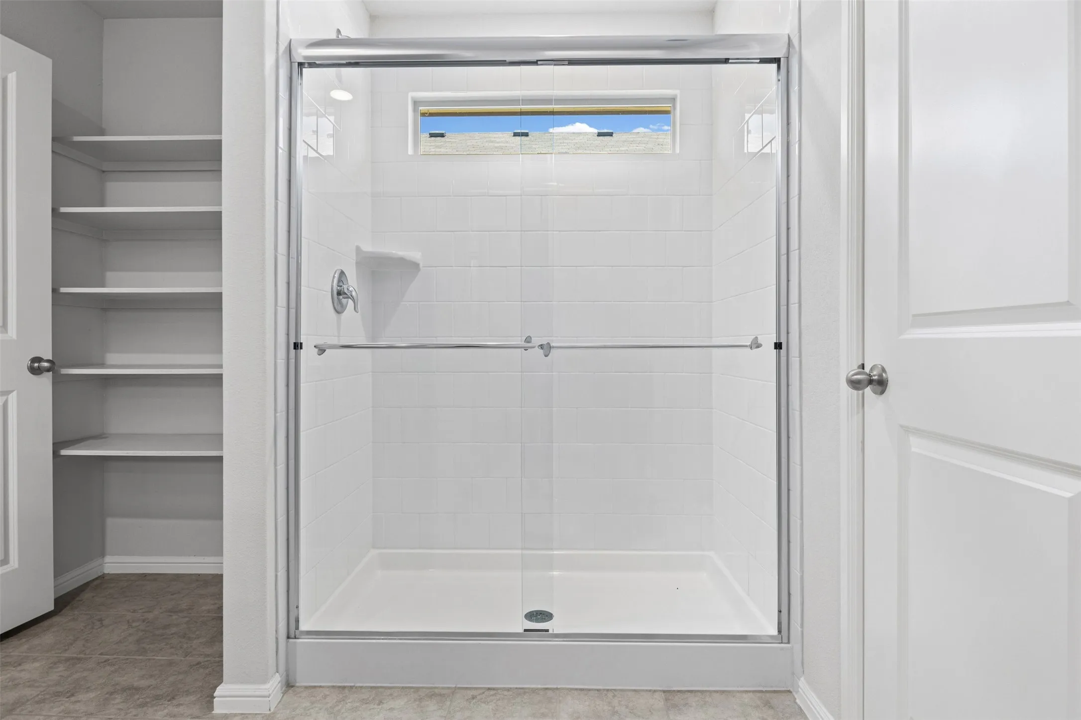 Glass-enclosed shower with white subway tile surround, integrated shelving, and a transom window