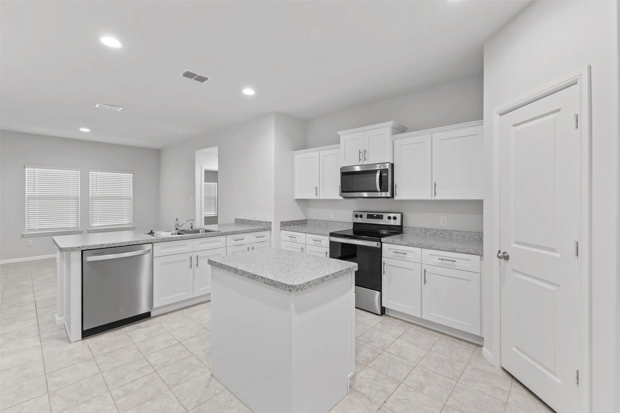 Open-concept kitchen featuring an island, white cabinetry, integrated stainless steel appliances, granite-style countertops, and tiled flooring