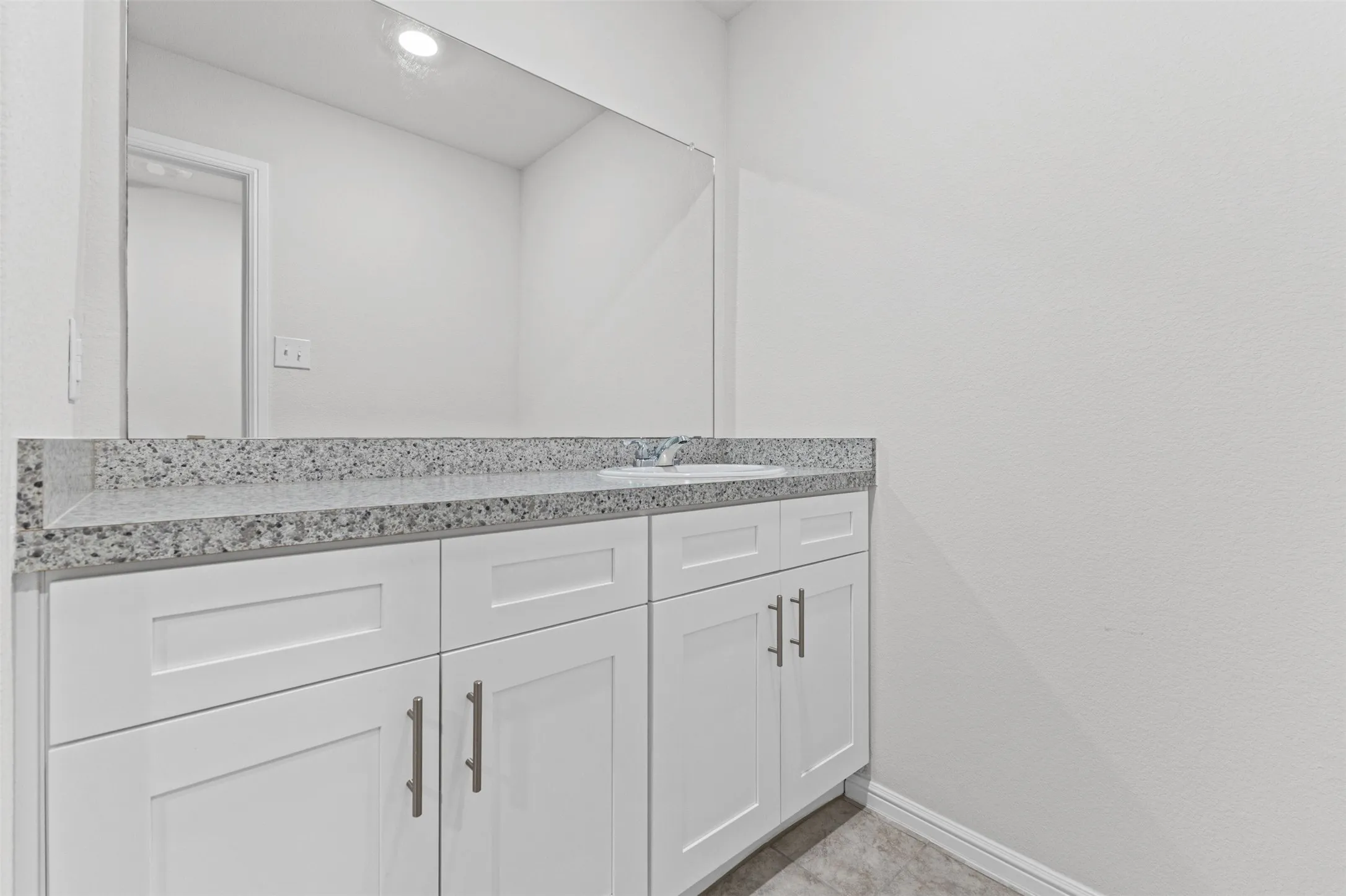 Bathroom vanity featuring a speckled countertop, integrated sink, and white shaker-style cabinetry with brushed nickel hardware