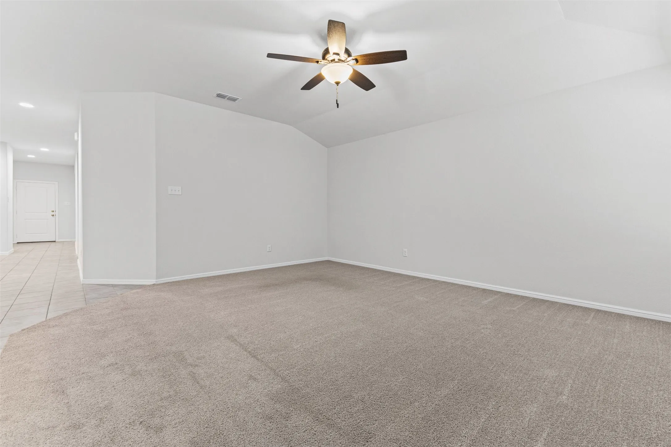 Spacious room featuring plush carpet flooring, a ceiling fan with integrated lighting, and a tray ceiling